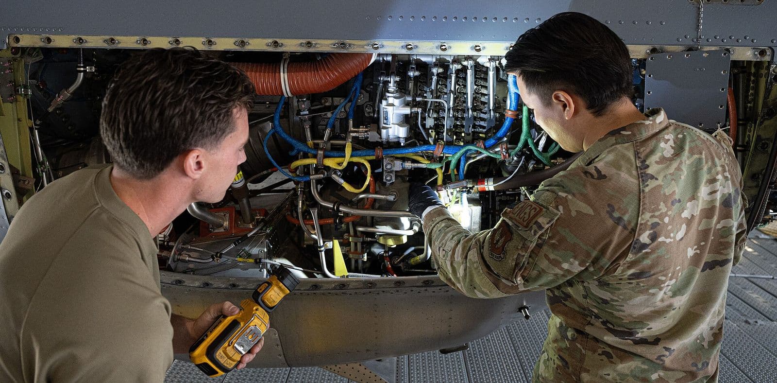 Two aerospace propulsion technicians inspect the open engine bay of a C-130J transport inside a maintenance hangar