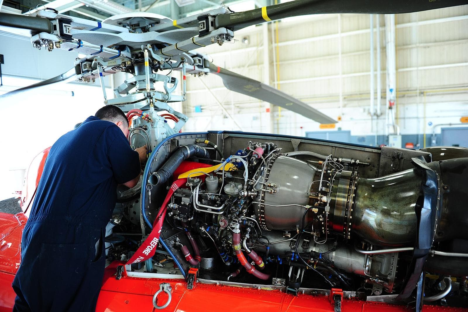 A Coast Guard aviation maintenance technician services the engine of an orange MH-65 helicopter in a hangar